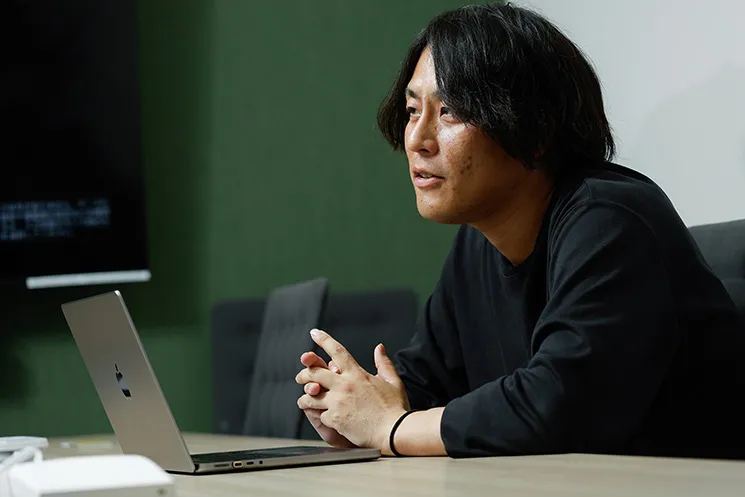 年々増加するソフトウエア脆弱性と優先順位付けの課題について語る、株式会社grasysの吉田悠介さん。ノートPCを開き、手を組んでインタビューに応える姿