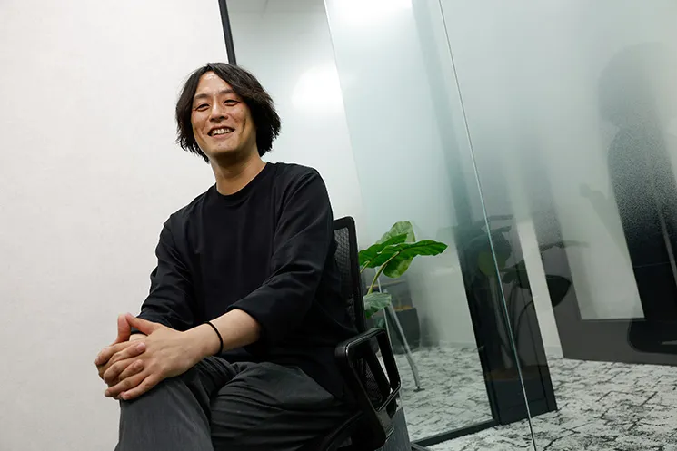株式会社grasysの吉田悠介さんのインタビュープロフィール写真。オフィスのミーティングスペースで椅子に座り、笑顔でカメラを見ている様子